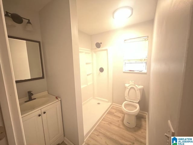 bathroom with baseboards, toilet, wood finished floors, vanity, and a shower stall