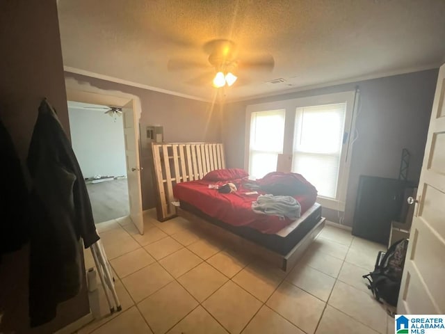 bedroom featuring crown molding, light tile patterned floors, visible vents, a ceiling fan, and a textured ceiling