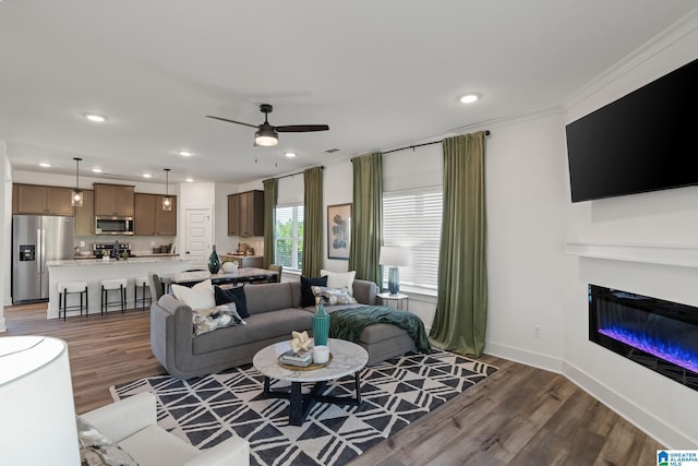 living area with recessed lighting, a ceiling fan, a glass covered fireplace, wood finished floors, and baseboards