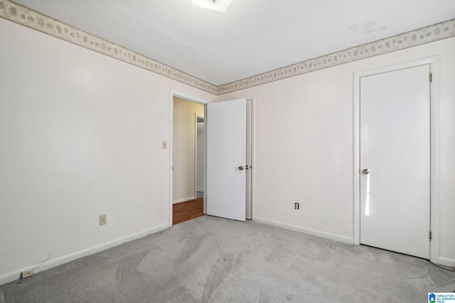 empty room with light colored carpet, a textured ceiling, and baseboards