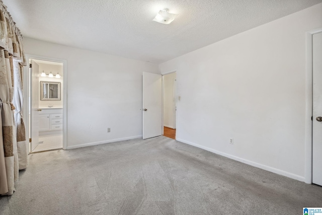 unfurnished bedroom with connected bathroom, baseboards, a textured ceiling, and light colored carpet