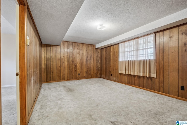 empty room with carpet, baseboards, wooden walls, and a textured ceiling