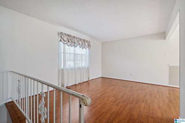 interior space with a textured ceiling, baseboards, and wood finished floors