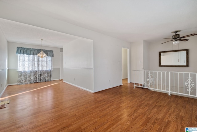 unfurnished room featuring baseboards, wood finished floors, and ceiling fan with notable chandelier