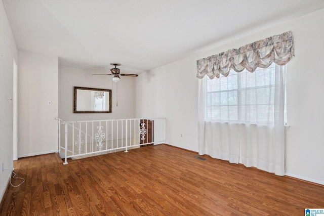 unfurnished room featuring a ceiling fan, visible vents, baseboards, and wood finished floors