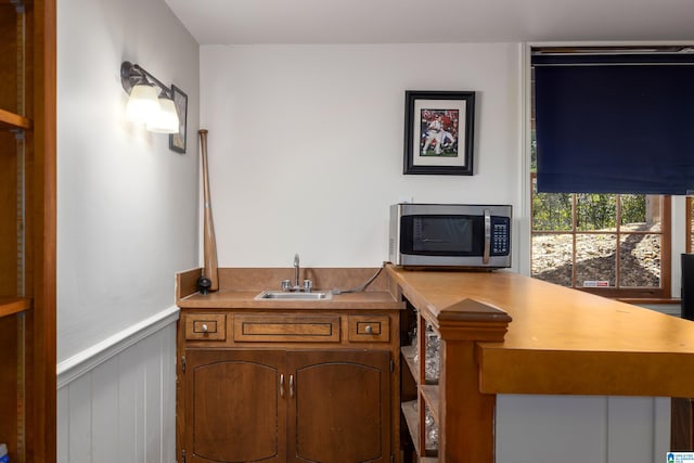 interior space featuring brown cabinetry, wainscoting, stainless steel microwave, a peninsula, and a sink