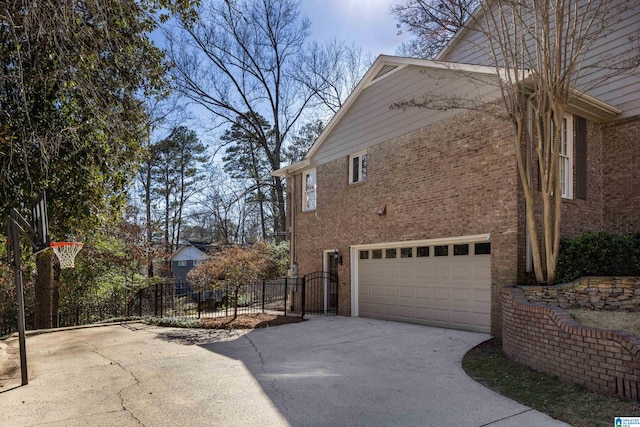 view of property exterior with driveway, a garage, a gate, fence, and brick siding