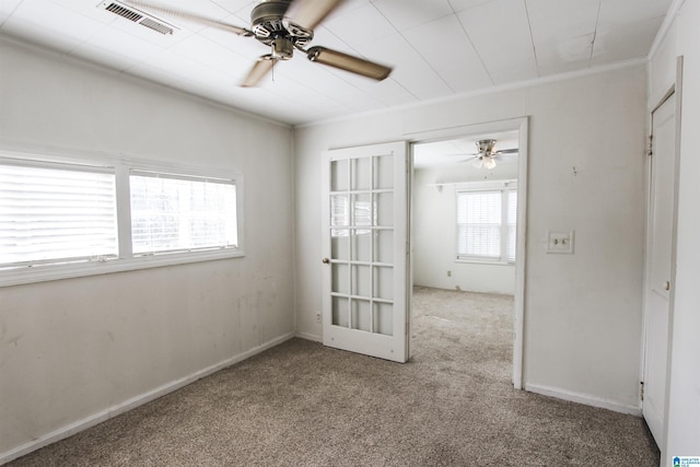 carpeted empty room with ceiling fan, crown molding, visible vents, and baseboards