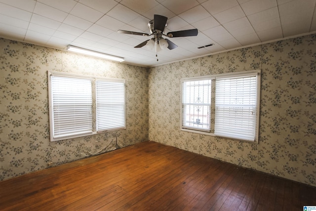 unfurnished room with wallpapered walls, a ceiling fan, visible vents, and hardwood / wood-style floors