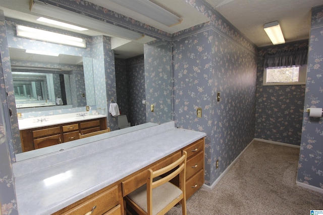 bathroom featuring double vanity, baseboards, and wallpapered walls