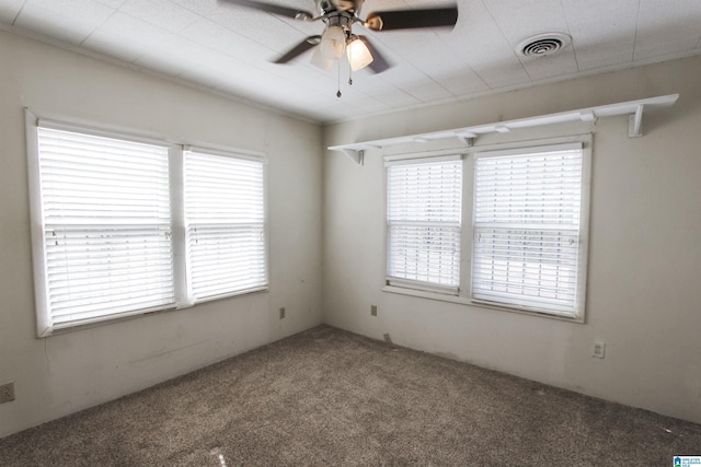 carpeted empty room featuring plenty of natural light, visible vents, and a ceiling fan