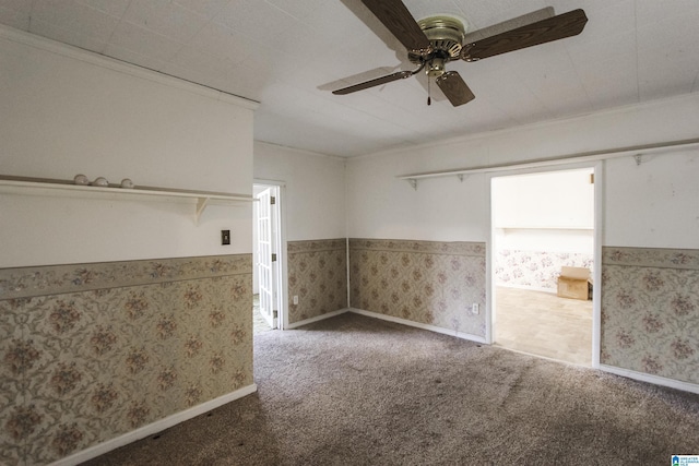 unfurnished room featuring wallpapered walls, baseboards, wainscoting, ceiling fan, and carpet