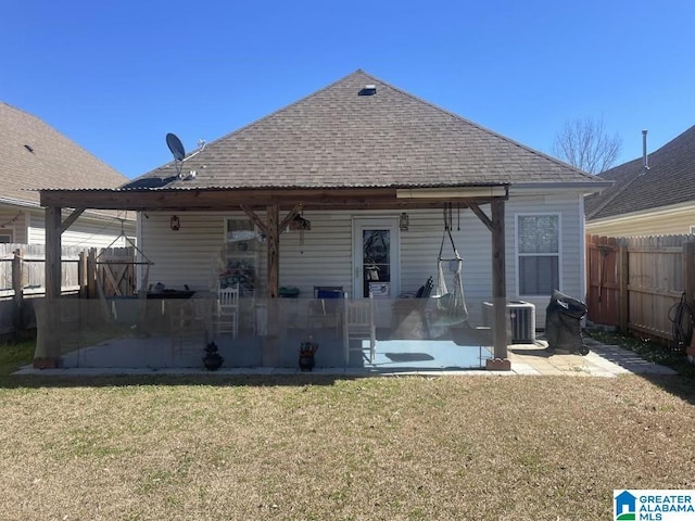 rear view of property featuring a shingled roof, central AC unit, a lawn, a patio, and fence