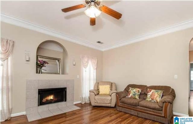 living area featuring ornamental molding, a fireplace, wood finished floors, and a ceiling fan