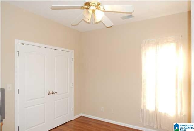 unfurnished bedroom with ceiling fan, multiple windows, baseboards, and wood finished floors