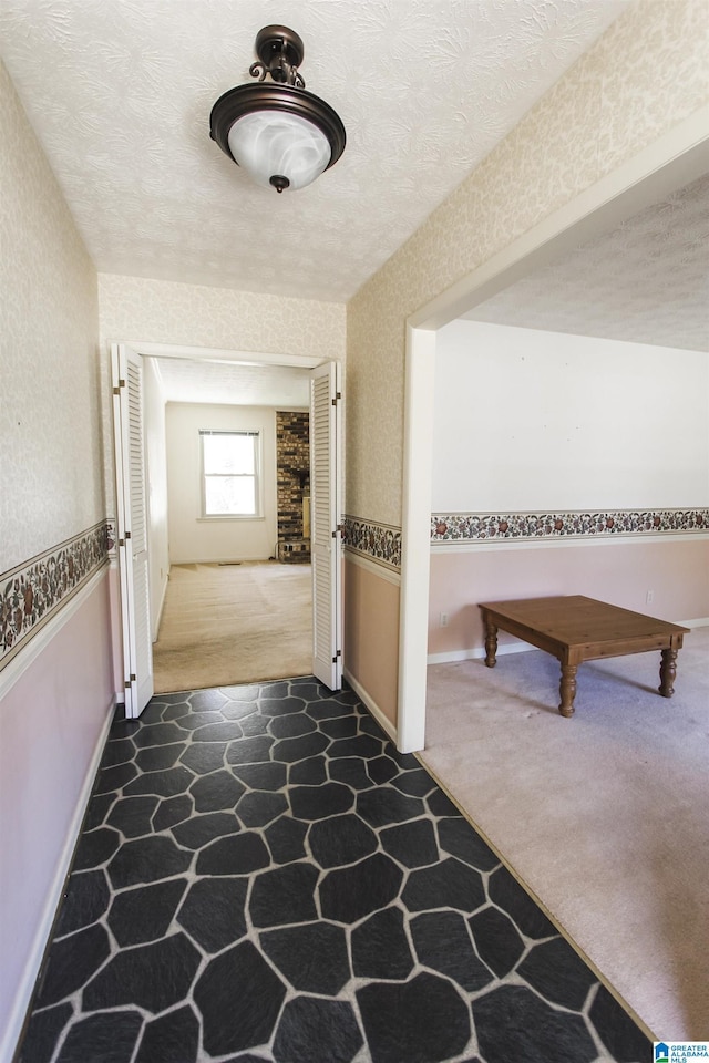 hall with carpet floors, a wainscoted wall, a textured ceiling, and wallpapered walls