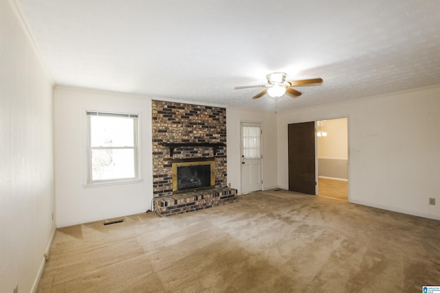 unfurnished living room with ceiling fan, a fireplace, visible vents, carpet, and crown molding