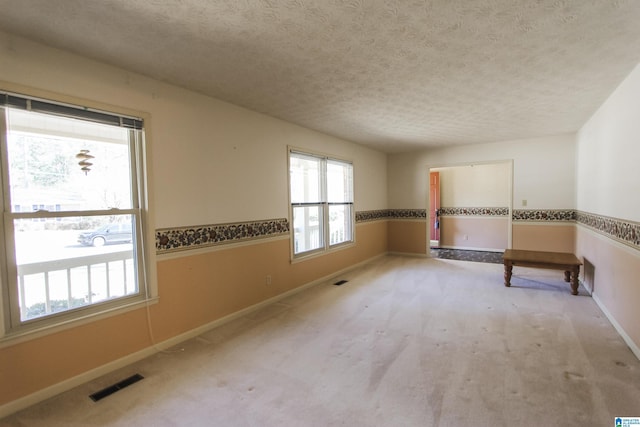 unfurnished room with carpet, visible vents, a textured ceiling, and baseboards