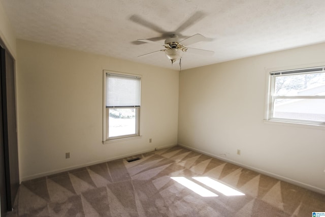 unfurnished room with a ceiling fan, carpet, visible vents, and plenty of natural light