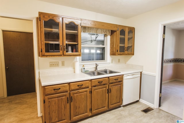 kitchen featuring visible vents, brown cabinetry, dishwasher, light countertops, and a sink