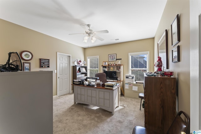 office space with light carpet, a wealth of natural light, visible vents, and a ceiling fan