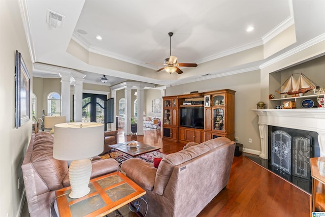 living area with a fireplace, visible vents, a ceiling fan, a tray ceiling, and decorative columns