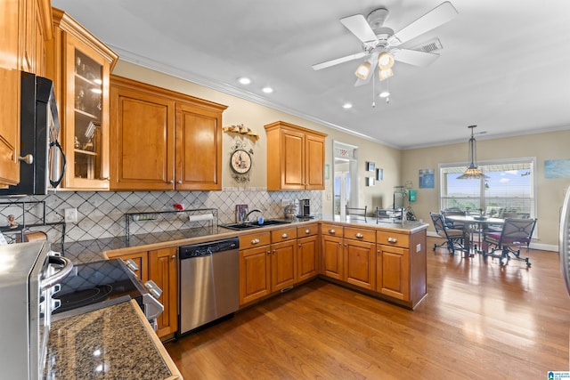 kitchen featuring brown cabinets, appliances with stainless steel finishes, a sink, wood finished floors, and a peninsula