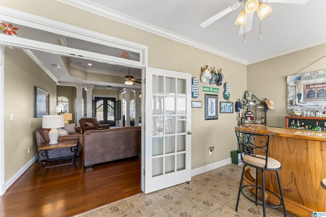 bar with a bar, ornamental molding, a ceiling fan, and ornate columns