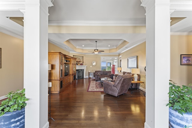 living room with decorative columns, ceiling fan, dark wood-type flooring, a tray ceiling, and a fireplace