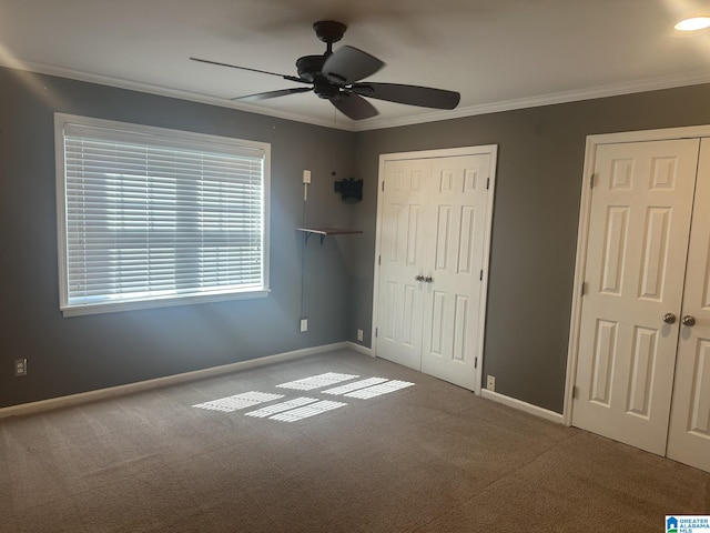 unfurnished bedroom featuring carpet flooring, a ceiling fan, baseboards, multiple closets, and crown molding