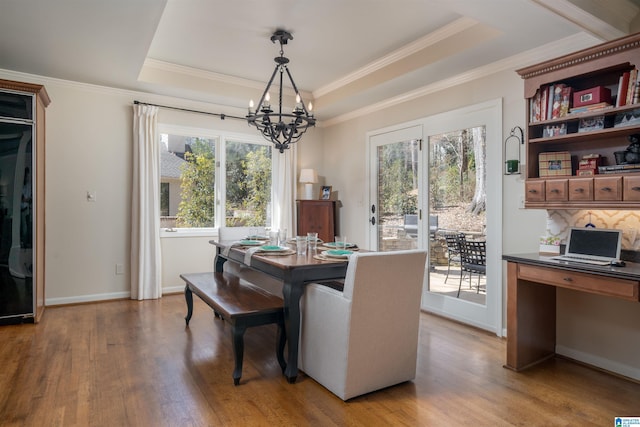 dining room with a notable chandelier, a raised ceiling, built in study area, wood finished floors, and baseboards