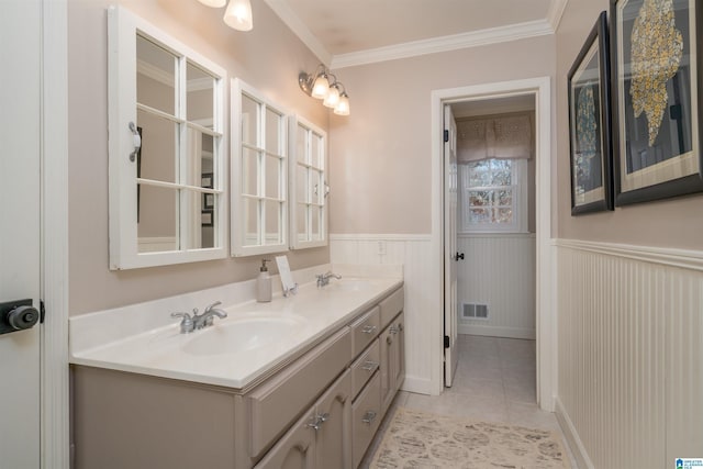 full bath with double vanity, a wainscoted wall, ornamental molding, tile patterned floors, and a sink