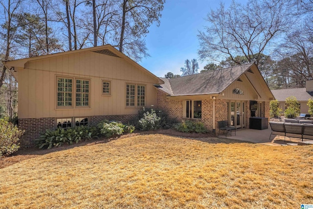 back of house with a shingled roof, a lawn, a patio, and brick siding