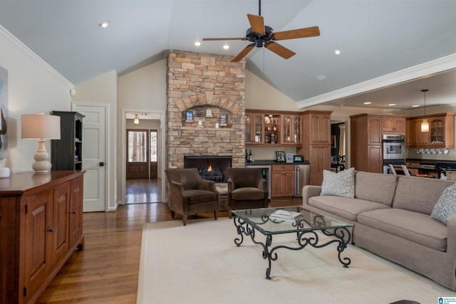 living area with high vaulted ceiling, a fireplace, wood finished floors, a ceiling fan, and ornamental molding