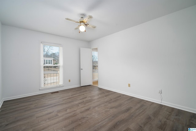 unfurnished room featuring dark wood-style floors, visible vents, baseboards, and a ceiling fan