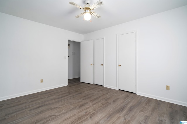 unfurnished bedroom with baseboards, ceiling fan, wood finished floors, and multiple closets