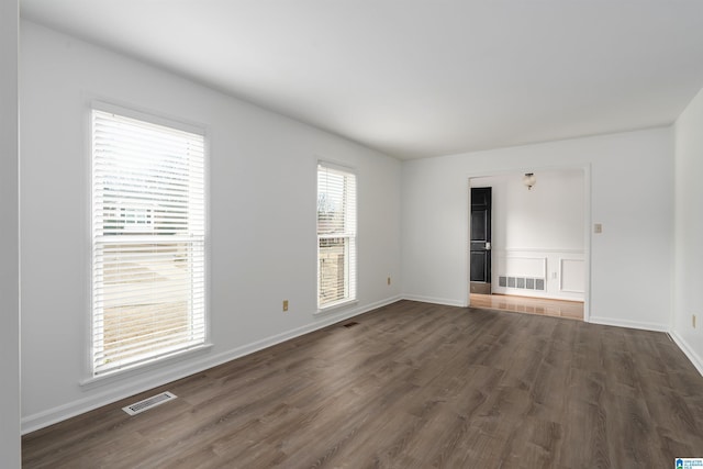 spare room featuring dark wood-style flooring, visible vents, and baseboards