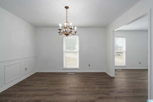 empty room with baseboards, dark wood-style flooring, visible vents, and a notable chandelier