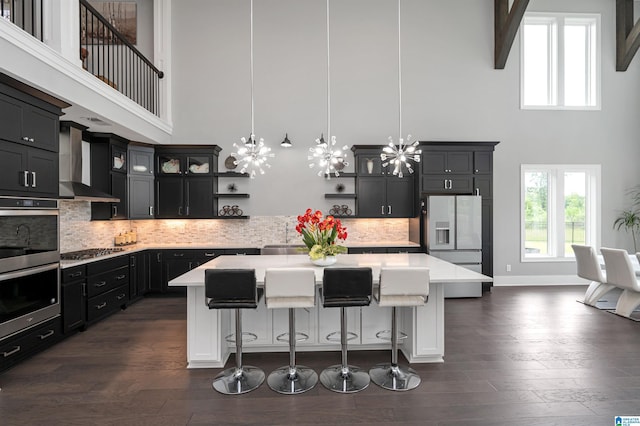 kitchen featuring light countertops, wall chimney range hood, appliances with stainless steel finishes, dark wood-style floors, and open shelves