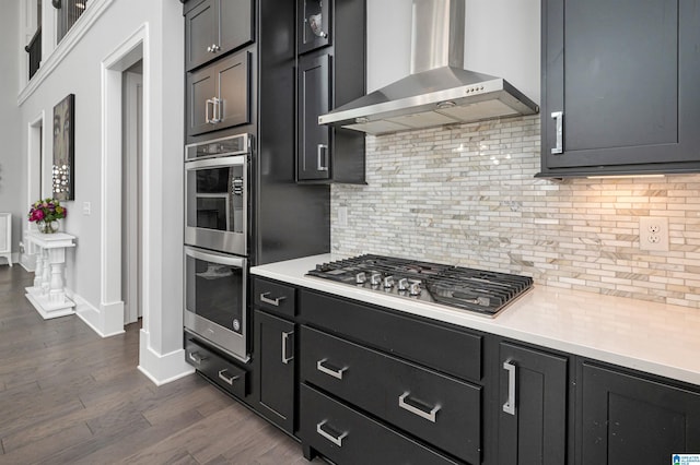 kitchen with wall chimney exhaust hood, appliances with stainless steel finishes, tasteful backsplash, and light countertops