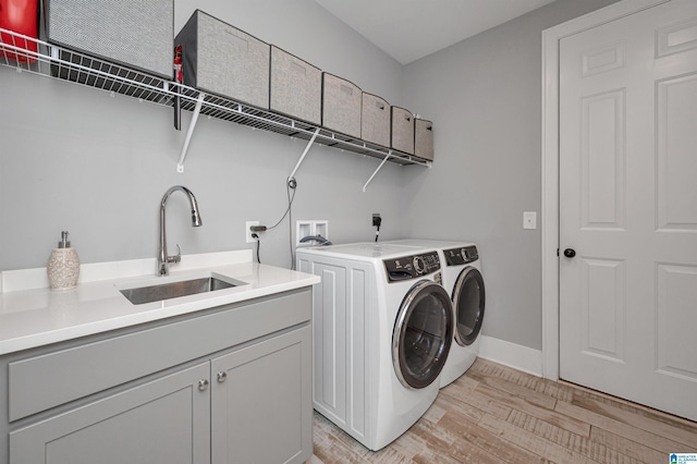 laundry area with cabinet space, baseboards, washing machine and clothes dryer, light wood-type flooring, and a sink