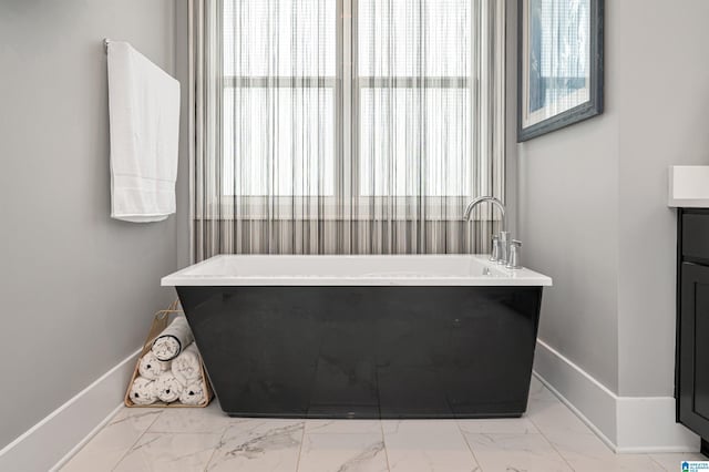 bathroom with marble finish floor, a freestanding bath, vanity, and baseboards