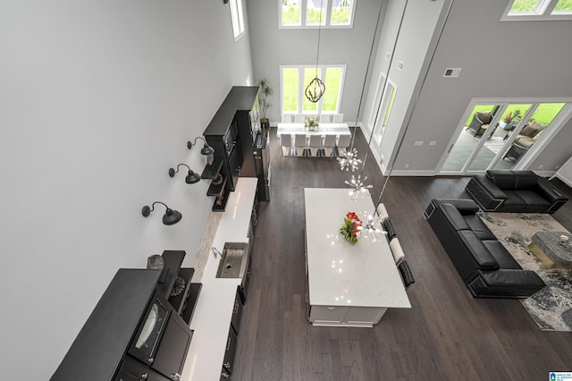 living room with a chandelier, dark wood-type flooring, visible vents, a towering ceiling, and baseboards