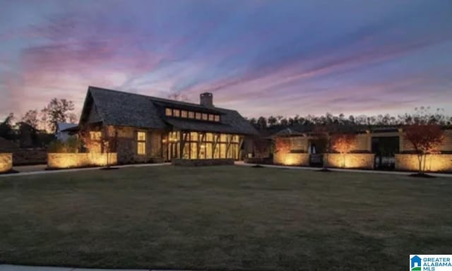 back of house at dusk with a yard and a chimney