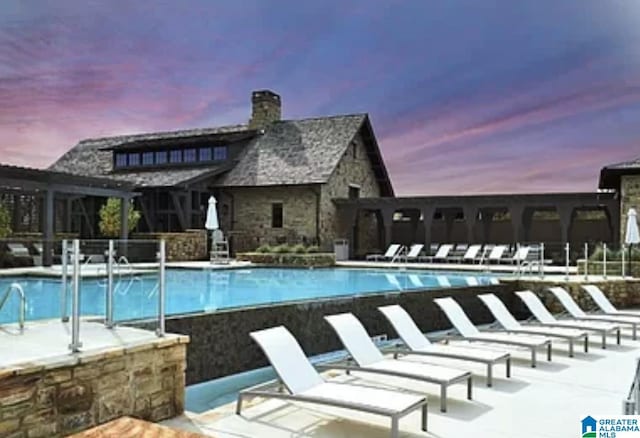 pool at dusk featuring a patio and a community pool