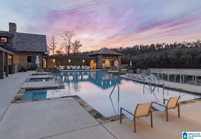 pool at dusk featuring a patio area and a community pool