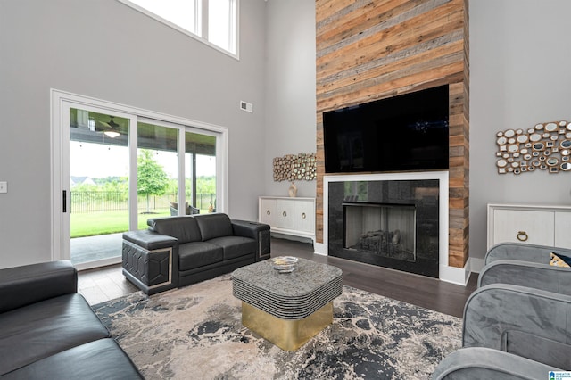 living area with a high ceiling, visible vents, a tiled fireplace, and wood finished floors