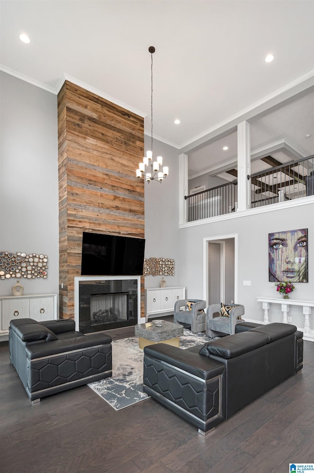 living area with a towering ceiling, ornamental molding, wood finished floors, a fireplace, and a chandelier