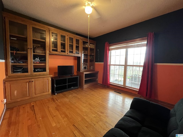 living area with a textured ceiling, a wainscoted wall, light wood-type flooring, and visible vents