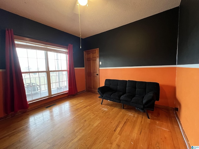 living area featuring a wainscoted wall, visible vents, a textured ceiling, and wood finished floors